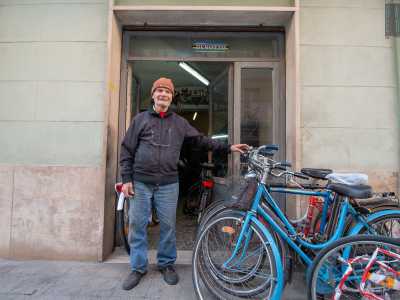 Lui ci aspetta fuori, davanti una porta a vetri senza insegna, davanti alla quale sono parcheggiate alcune due ruote di colore azzurro e rosso